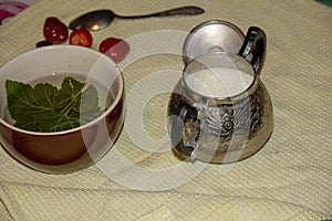 On the table is a Mug, sugar bowl, spoon and strawberry. In a mug lies a piece of currant and poured tea. tea time