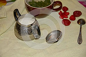 On the table is a Mug, sugar bowl, spoon and strawberry. In a mug lies a piece of currant and poured tea. tea time