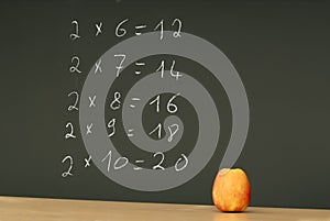 Table multiplication on blackboard desk with apple