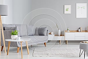 Table next to grey sofa in scandi living room interior with post