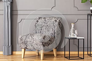 Table next to patterned grey armchair against wall with molding