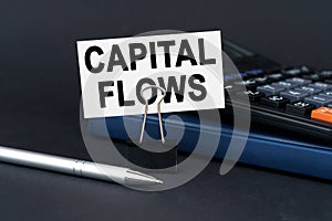 On the table is a notebook, a calculator, a pen and a business card with the inscription - Capital Flows