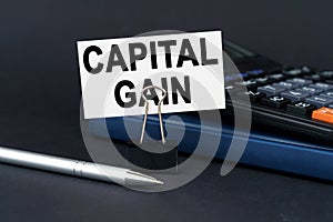 On the table is a notebook, a calculator, a pen and a business card with the inscription - capital gain