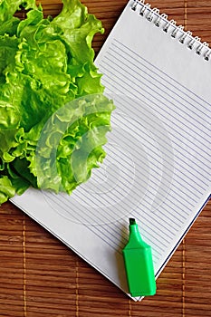 On the table is a notebook, marker and fresh lettuce leaves photo