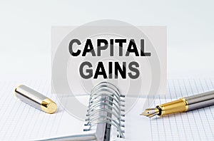 On the table is a notebook, a pen and a business card with the inscription - CAPITAL GAINS