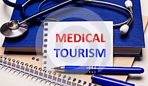 On the table are notepads, a stethoscope, a pen and a sheet of paper with the text MEDICAL TOURISM. Medical concept