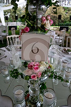 Table number stand of a luxury alfresco wedding reception at the countryside; top table flower arrangements, crystal center piece