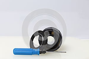 On the table is an old disassembled lens and a screwdriver. On a white background.