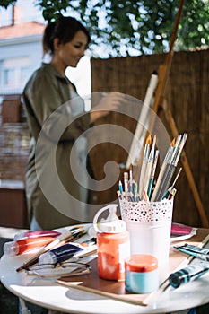 Table with paint tubes and brushes in front of blurred artist