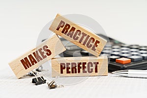 On the table is a pen, a calculator and small wooden blocks with the inscription - PRACTICE MAKES PERFECT