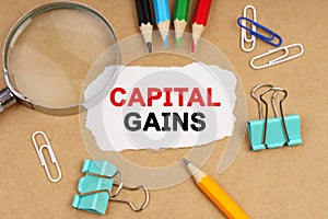 On the table are pencils, paper clips, a magnifying glass and paper with the inscription - CAPITAL GAINS