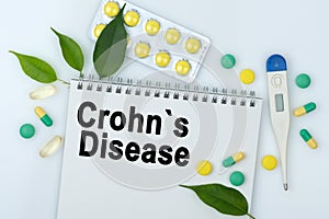 On the table are pills, a thermometer, leaves and a notebook with the inscription -Crohns Disease photo