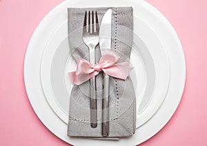 Table place setting in pink. Gray linen napkin with ribbon and white plates on pink color background