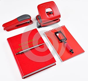 On the table are red office supplies: stapler, hole punch, Notepad, magnifier, book and pen