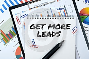 On the table are reports, charts, a notebook with the inscription - GET MORE LEADS