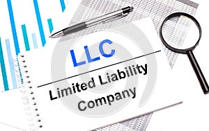 On the table are reports, diagrams, a pen, a magnifying glass and a white notepad with LLC Limited Liability Company. Business