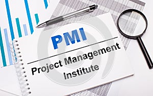 On the table are reports, diagrams, a pen, a magnifying glass and a white notepad with PMI Project Management Institute text.