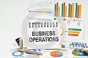 On the table are reports with graphs and a notepad with the inscription - Business Operations