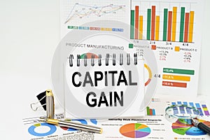 On the table are reports with graphs and a notepad with the inscription - capital gain