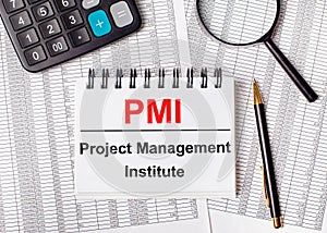 On the table are reports, a magnifying glass, a calculator, a pen, and a white notebook with the text PMI Project Management