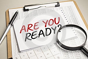 On the table are reports, a magnifying glass, a calculator, and a white notepad with the words ARE YOU READY . Business concept