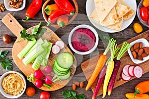 Table scene with a variety of fresh vegetables and hummus dips, overhead view on a wood background