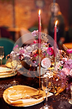 Table served for Christmas dinner, festive setting with decorations, burning candles and golden fern branches, glasses. Selected
