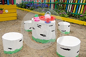 Table with set of children`s dishes for tea drinking and seat made of wooden chocks