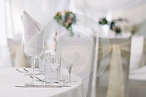 Table set for an event party or wedding reception on white tablecloth. White soft background with tables and flowers