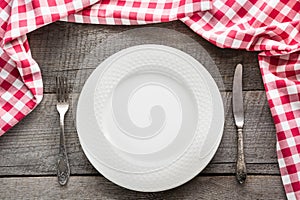 Table set with white plate with knife and fork with red napkin around .