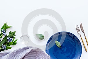 Table setting with blue plate, fork, knife and flower on white kitchen background top view mockup