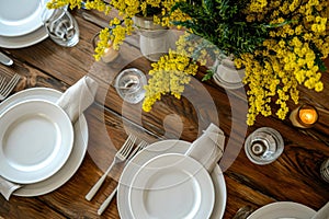 table setting. A bouquet of mimosa in a vase, plates and cutlery on a wooden table. top view.