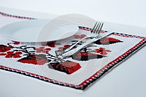 Table setting for dinner: a plate, a fork, a knife on a woven cloth napkin with an embroidered pattern,  traditional handmade in