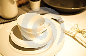Table setting. Dinner. A white cup stands on two white saucers on a table covered with a tablecloth. Next to it are cutlery in a