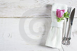 Table setting with handmade forged fork and knife, white linen napkin with ring and purple flower