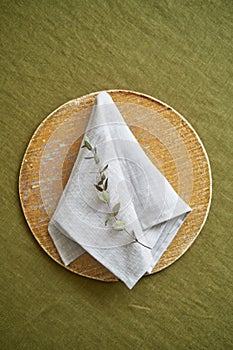 Table setting option. A linen grey napkin is neatly folded on a brown plate. Olive background.
