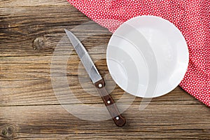 Table setting with red white napkin plate and knife on wooden table