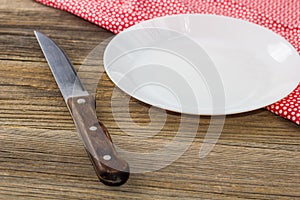 Table setting with red white napkin plate and knife on wooden table