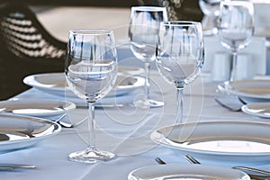 Table setting in restaurant. Empty wine glasses, plates, forks, knifes on the tablecloth. Elegant restaurant interior.