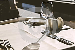 Table setting in restaurant. Empty wine glasses, plates, forks, knifes on the tablecloth. Elegant restaurant interior.