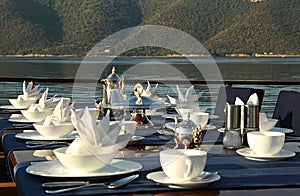 A table setting with silver teapot, cookie plate and accesories on the luxury big yacht in morning light.