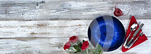 Table setting for Valentines Day celebration in flat lay format with blue plate, red roses, napkin, silverware and drinking glass