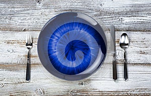 Table setting with vintage cutlery, empty blue plate, fork, spoon and knife on white rustic wood table