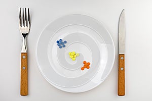 Table setting with a white plate filled with various capsules next to the cutlery on a white background.