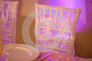 Table setup for a formal dining experience with focus on a white chair backrest covered in a thin, see-through silky cloth