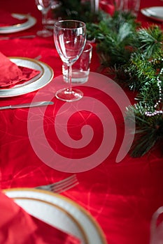 Table setup lunch in red for celebration. Shiny glass cup, red tablecloth, candles and decorations with green Christmas tree.