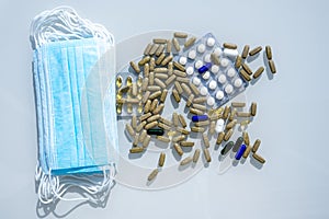 A table with several surgical masks. Assorted pharmaceutical medicine pills, tablets and capsules near the masks.