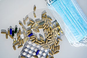 A table with several surgical masks. Assorted pharmaceutical medicine pills, tablets and capsules near the masks