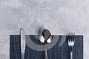 On the table is a spoon, fork and knife on a serving napkin.