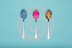 Table spoons filled with assortment of various colourful pills on blue pastel coloured background. Medication.